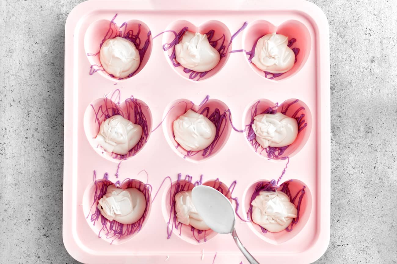 adding melted white candy wafers to heart shaped silicone mold