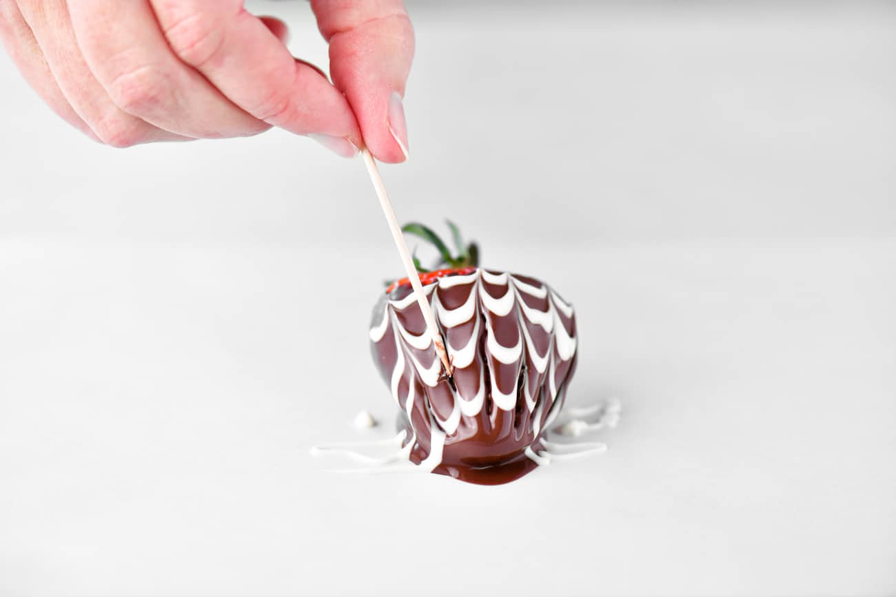 dragging a toothpick through the chocolate on the strawberry