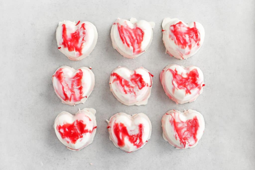 9 white and red heart shaped hot chocolate bombs on a sheet of parchment