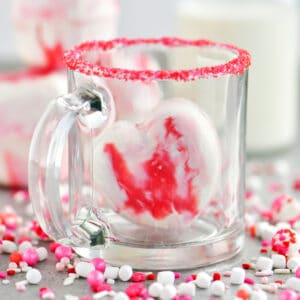 Heart shaped hot chocolate bomb in a clear glass mug.