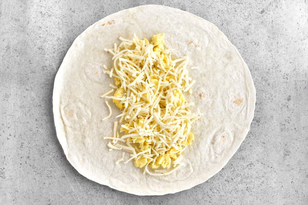 adding eggs and cheese to a tortilla