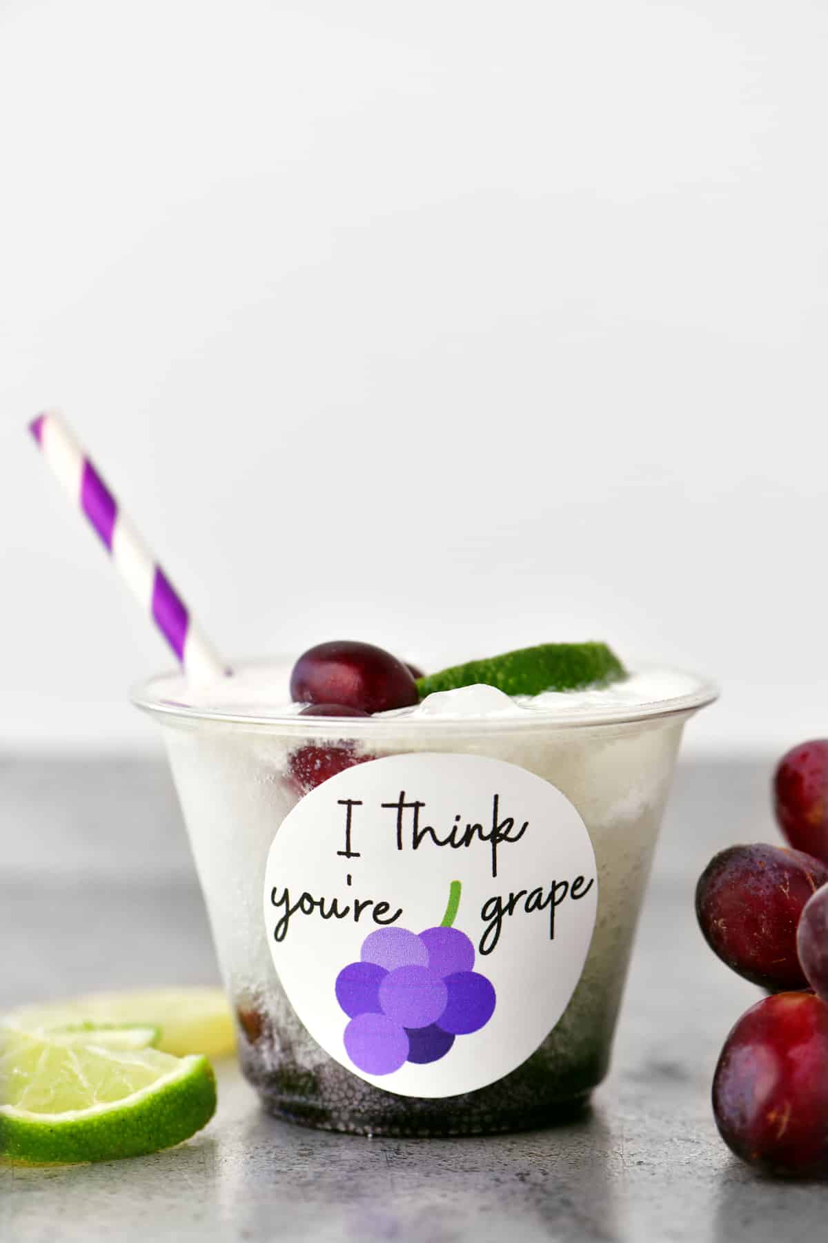 a grape flavored valentines drink in a clear cup with a purple and white striped straw