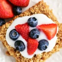 a topdown view of strawberries blueberries and yogurt on a slice of oatmeal bake
