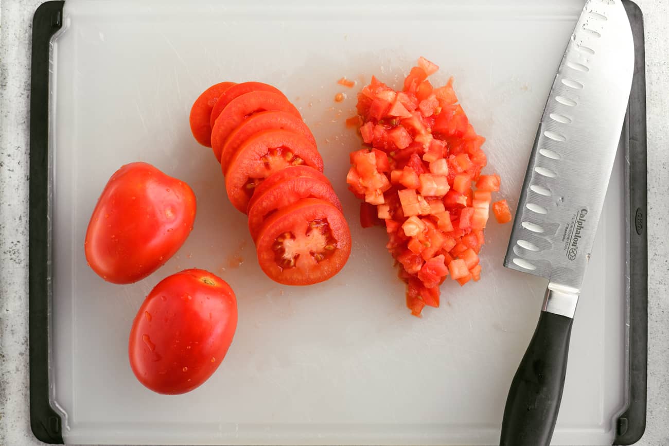 a knife, 2 whole tomatoes, alongside some sliced and diced tomatoes on a cutting board