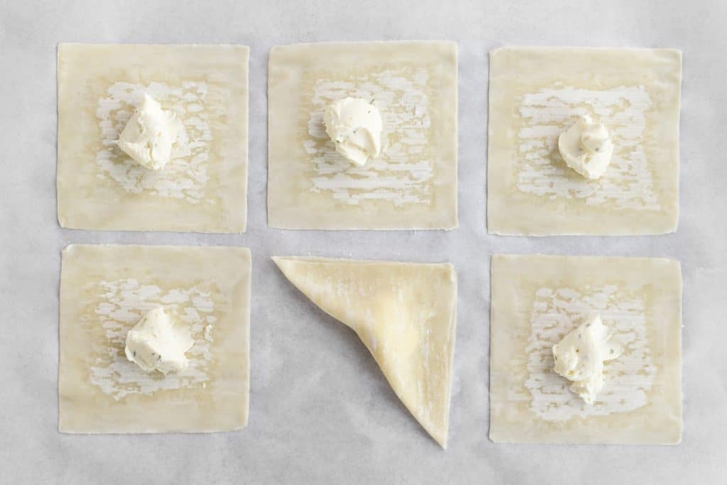 5 wonton wrappers with cream cheese filling on top, and one wrapper folded over the cream cheese