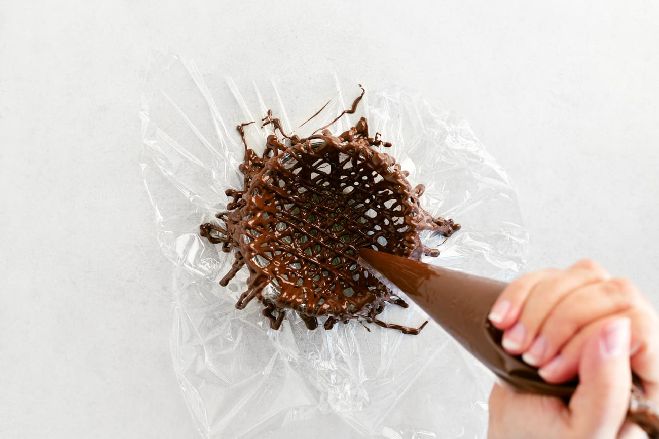 piping melted chocolate onto the plastic covered bowl
