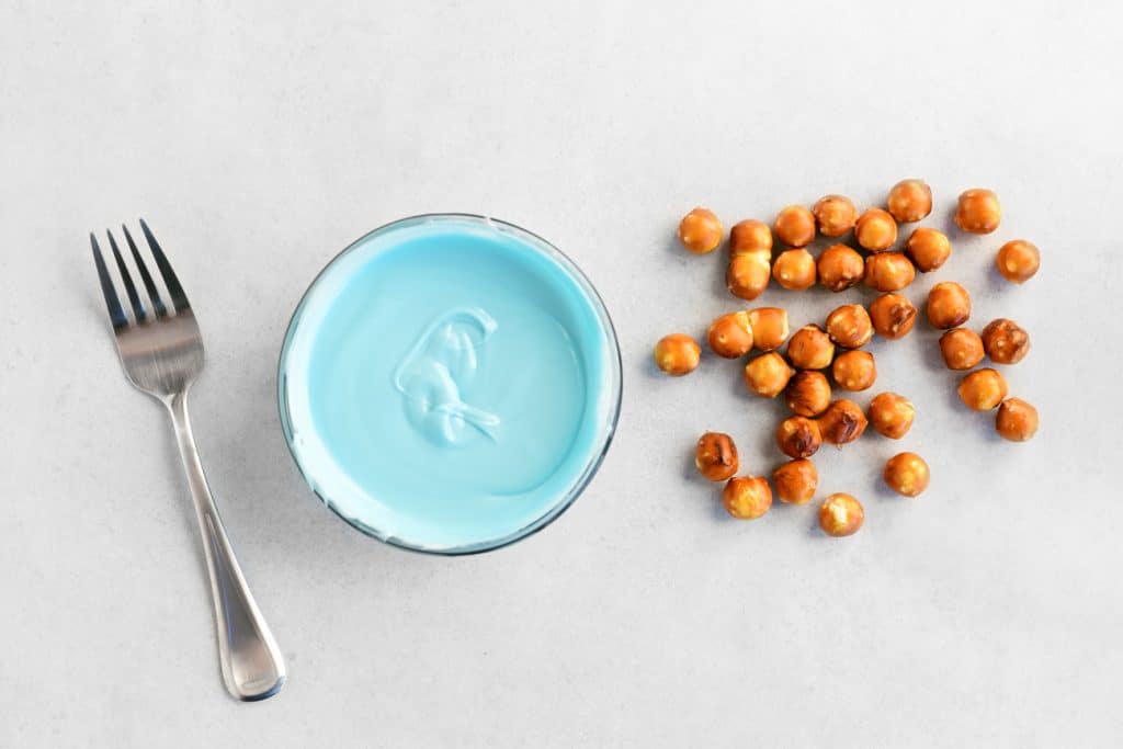 a fork, blue melted candy in a bowl, and pretzel nuggets on a sheet of parchment paper