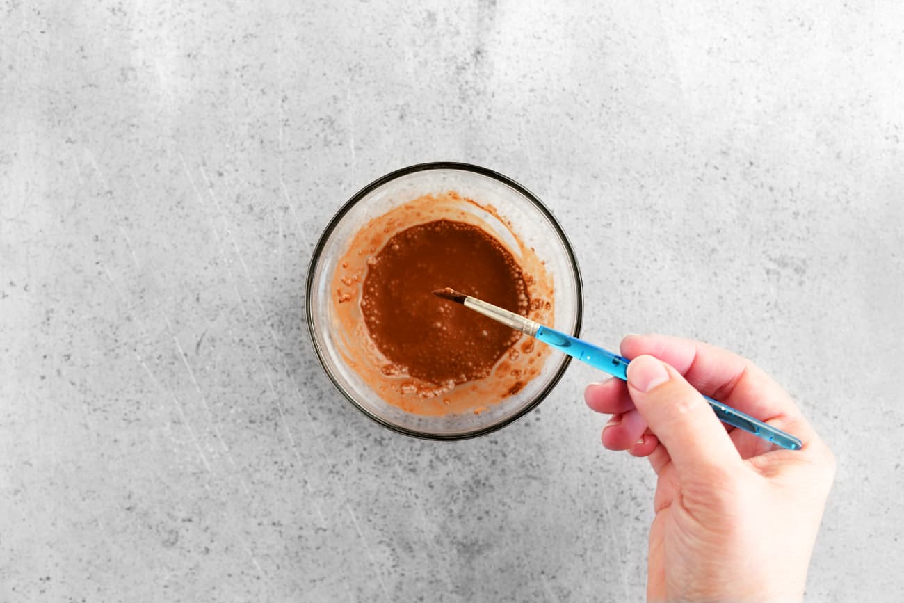 dipping a paint brush into a bowl of cocoa mixture