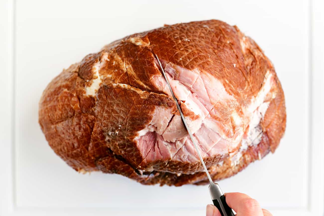 a handholding a carving knife which is scoring the ham
