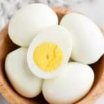 boiled eggs in a bowl, one egg is cut in half so you can see the yolk
