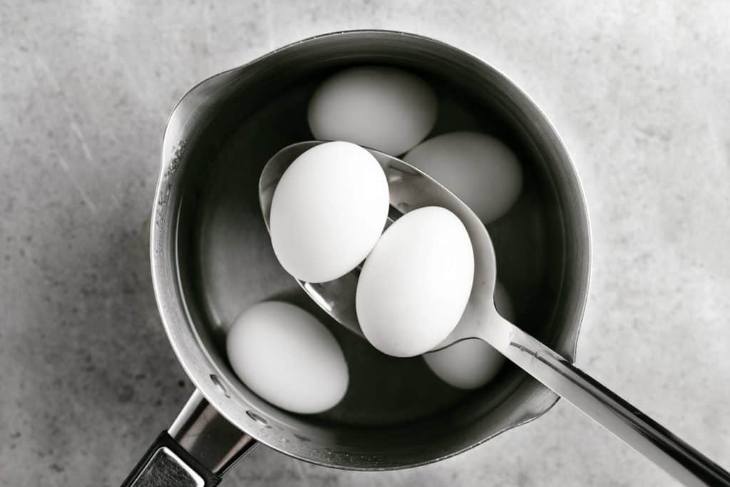 2 eggs on a spoon above a pot of water