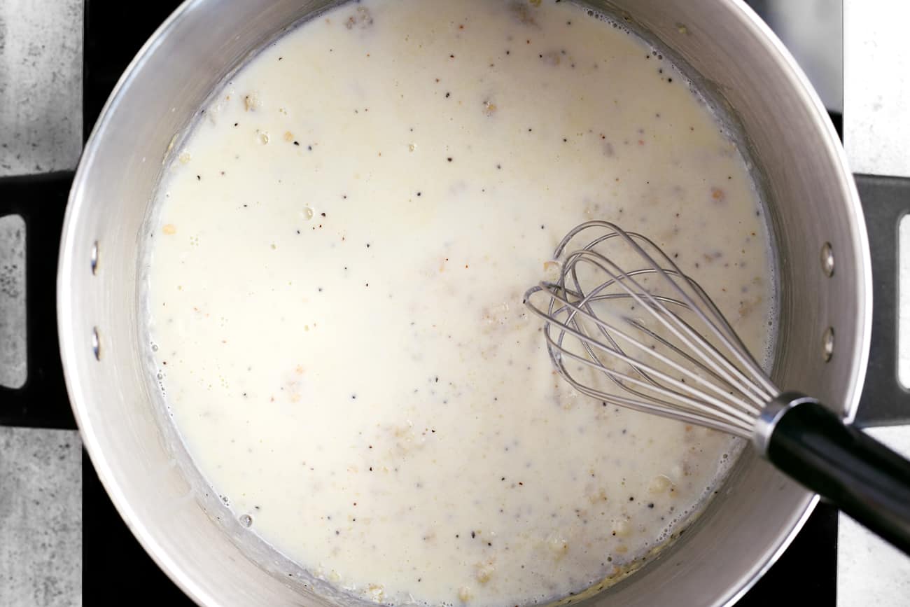 a whisk and the sauce for scalloped potatoes in a cooking pot