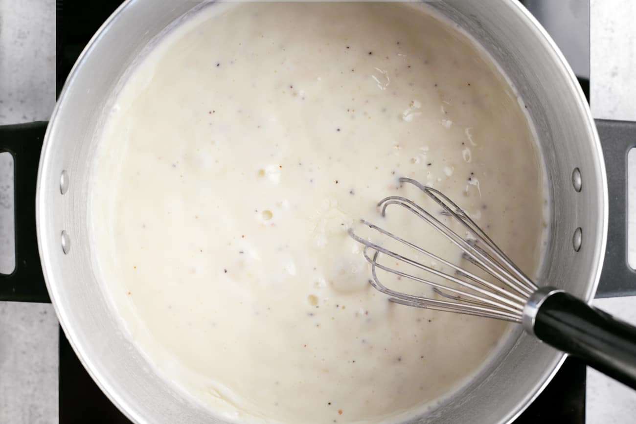 a whisk and the thickened sauce for scalloped potatoes in a cooking pot