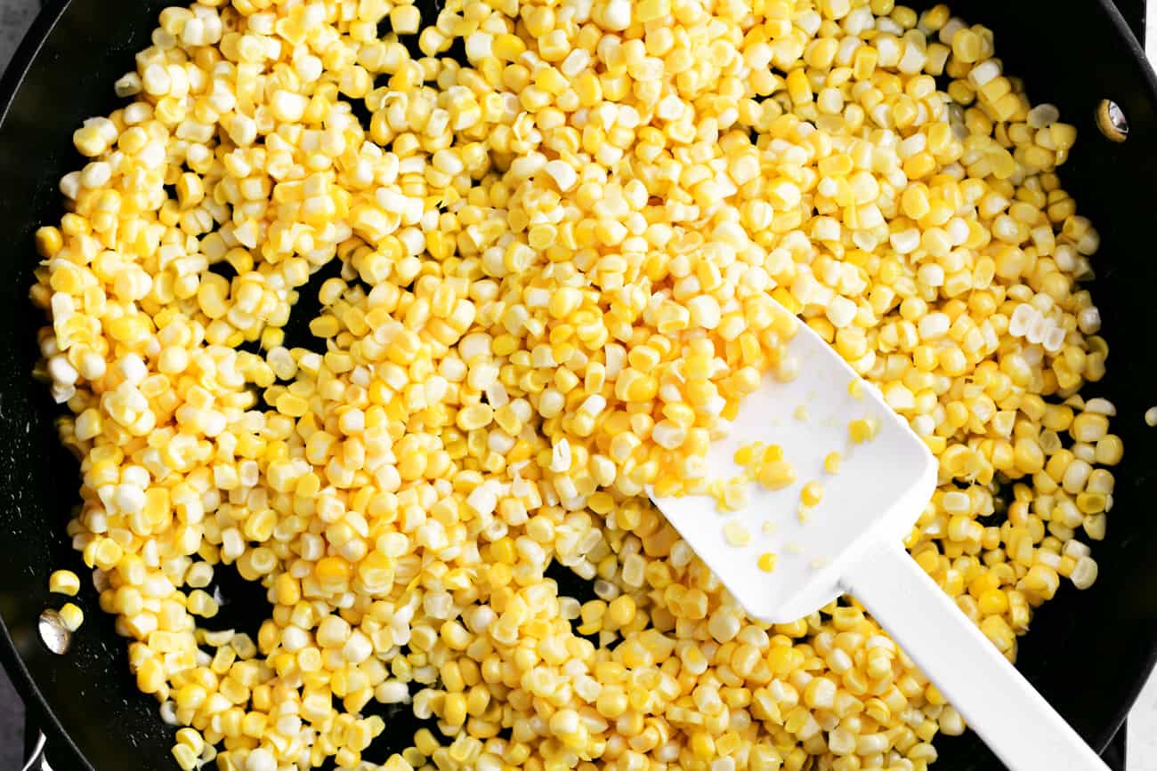 A white spoon-shaped spatula stirring kernels in a skillet.