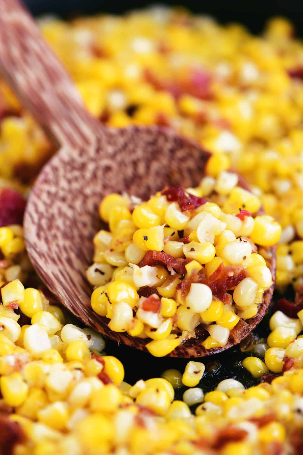 a wooden spoon with peppered corn and bacon in it