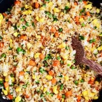 fried rice with eggs, peas and carrots in a pan with a wooden spoon