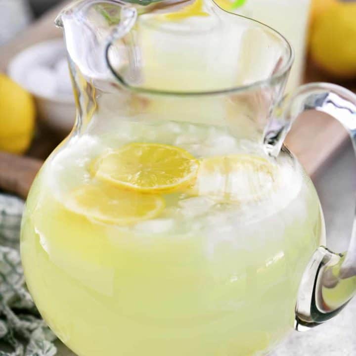 a glass pitcher with lemonade, lemon slices, and ice cubes