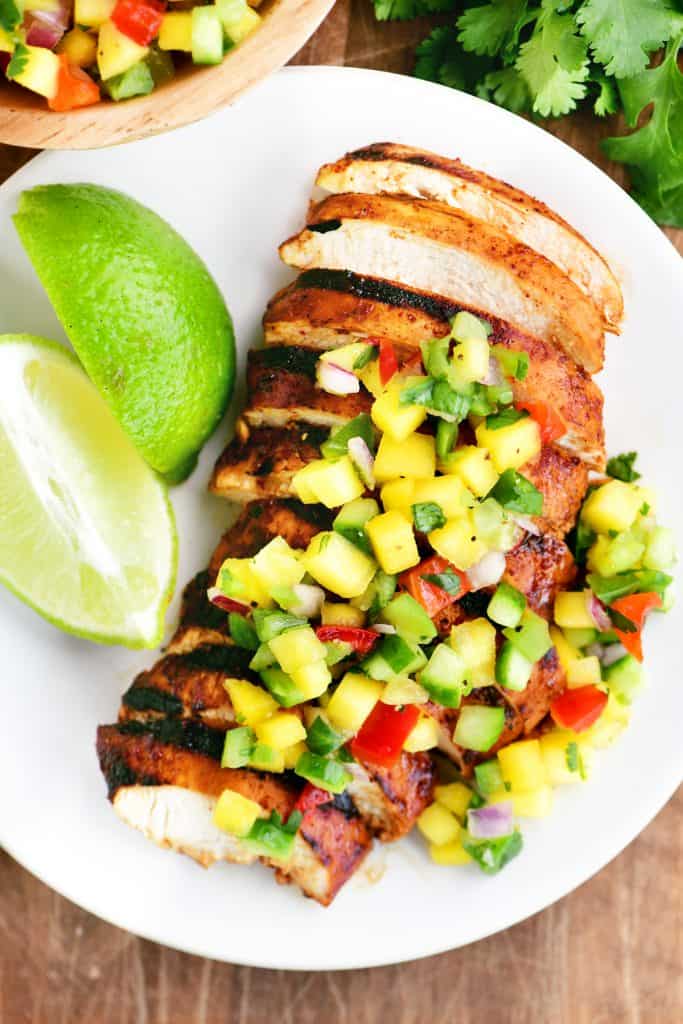 sliced mango chicken on a white plate with mango salsa on top