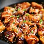 sesame chicken in a skillet with chives on top