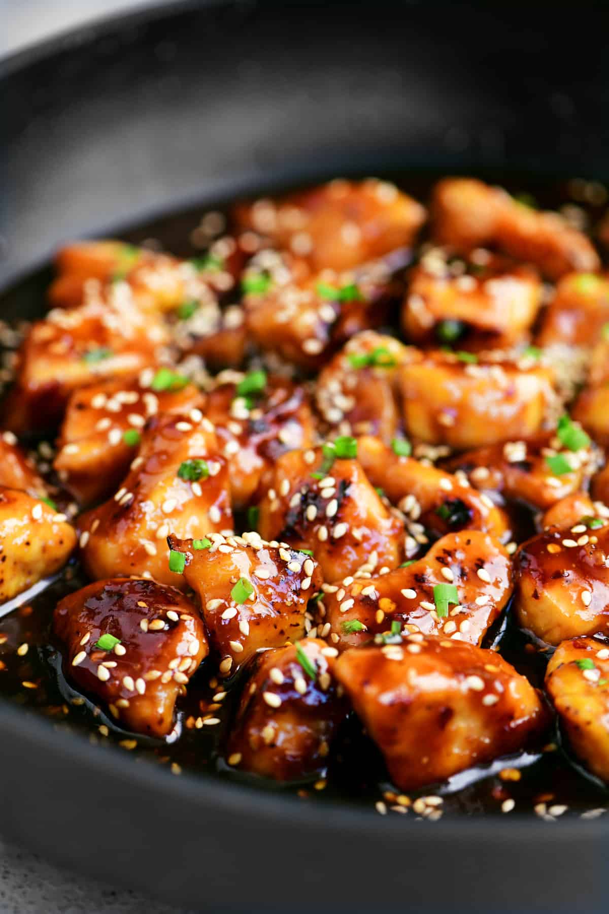 sesame chicken in a skillet with chives on top