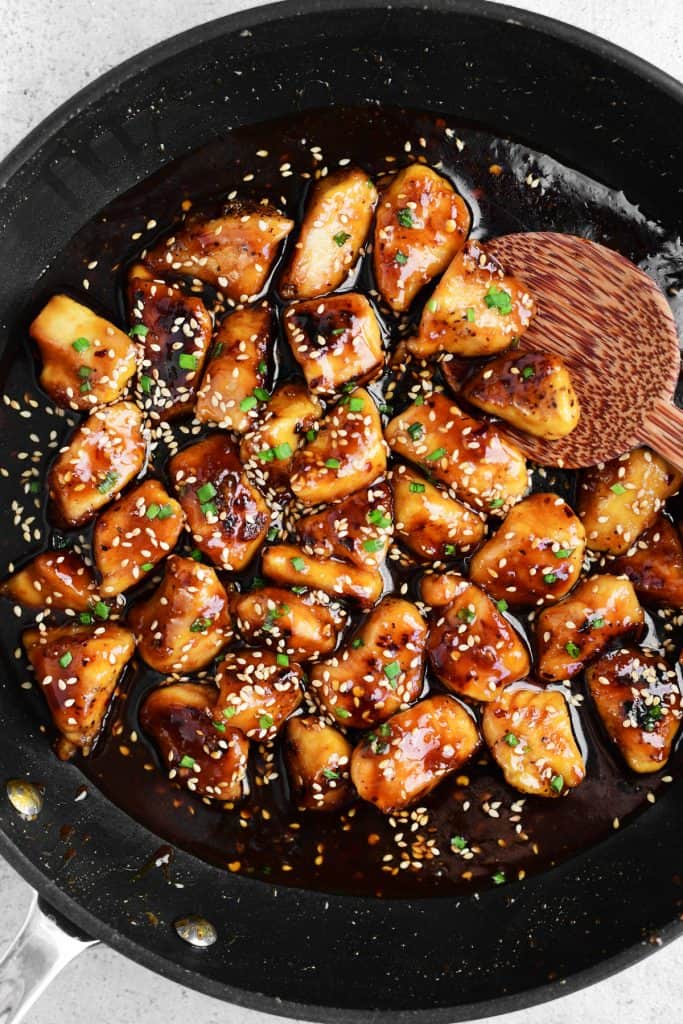 sesame chicken in a skillet with a wooden spoon