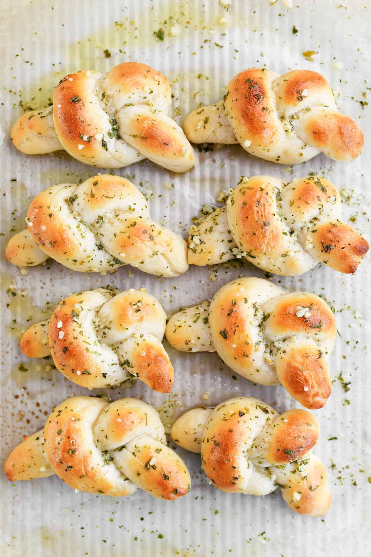 Eight garlic knots with butter and garlic on a pan.