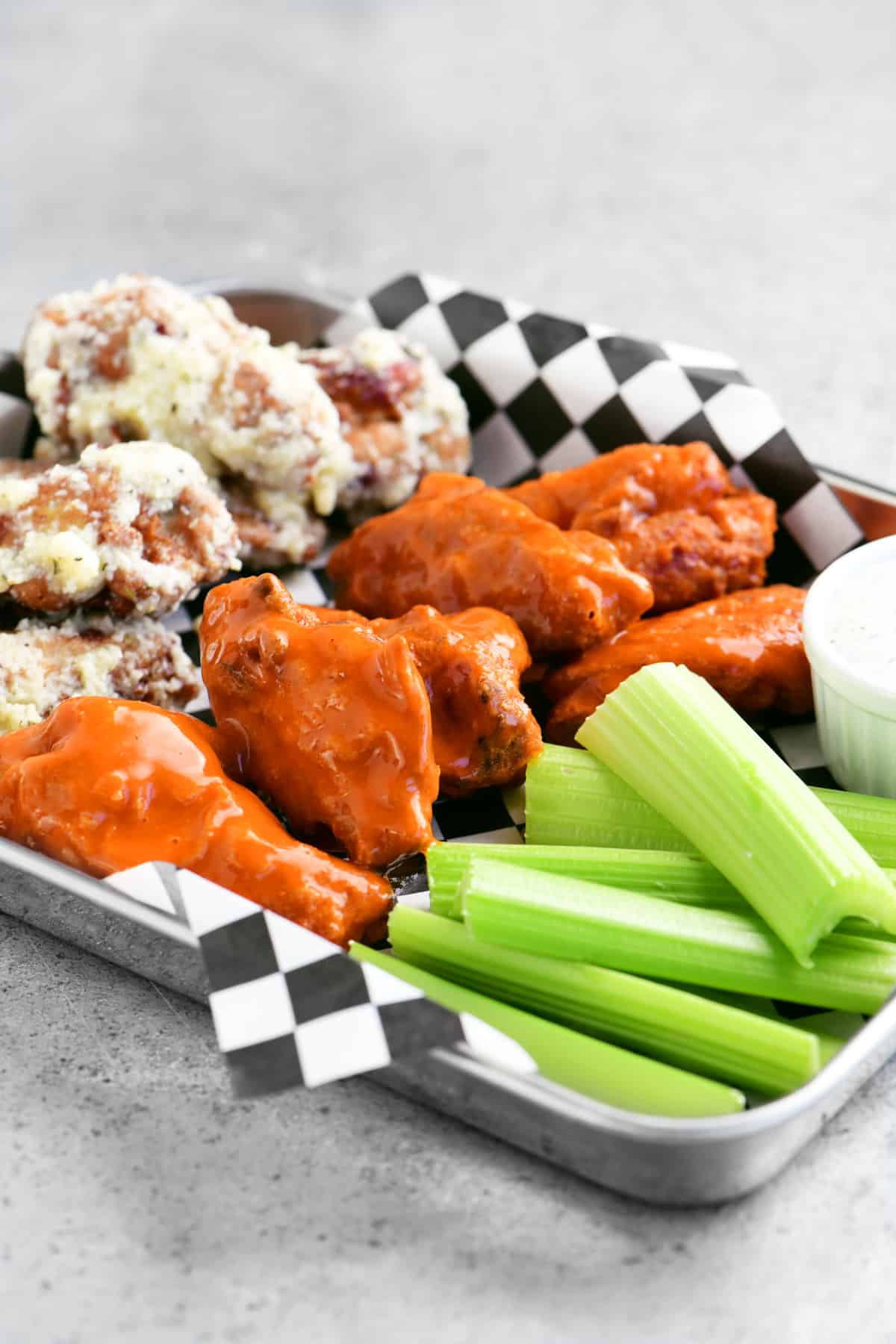 a stainless tray with buffalo wings and parmesan garlic wings and celery