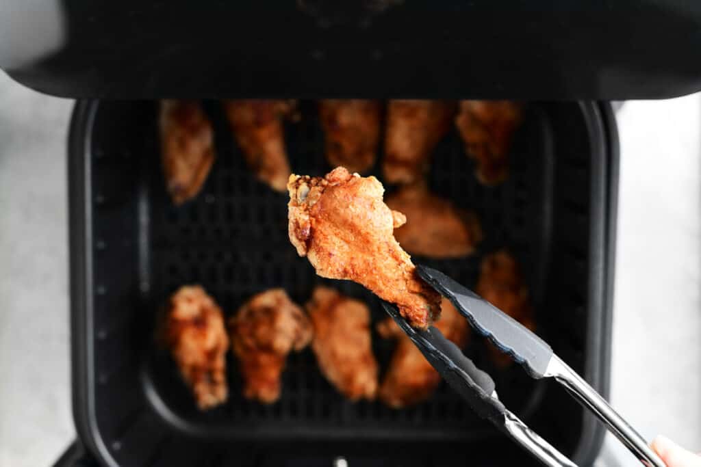 a pair of tongs lifting a chicken wing from the fryer basket