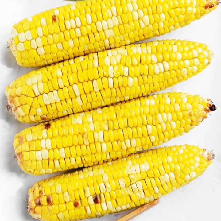 four ears of corn on a white platter with butter and salt