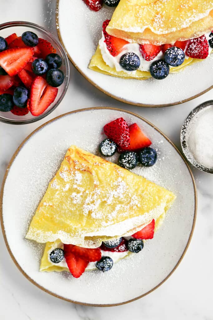 folded crepes with berries and whipped cream inside arranged on plates