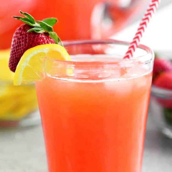 a glass of strawberry lemonade with a straw inside and a lemon and strawberry on the rim of the glass