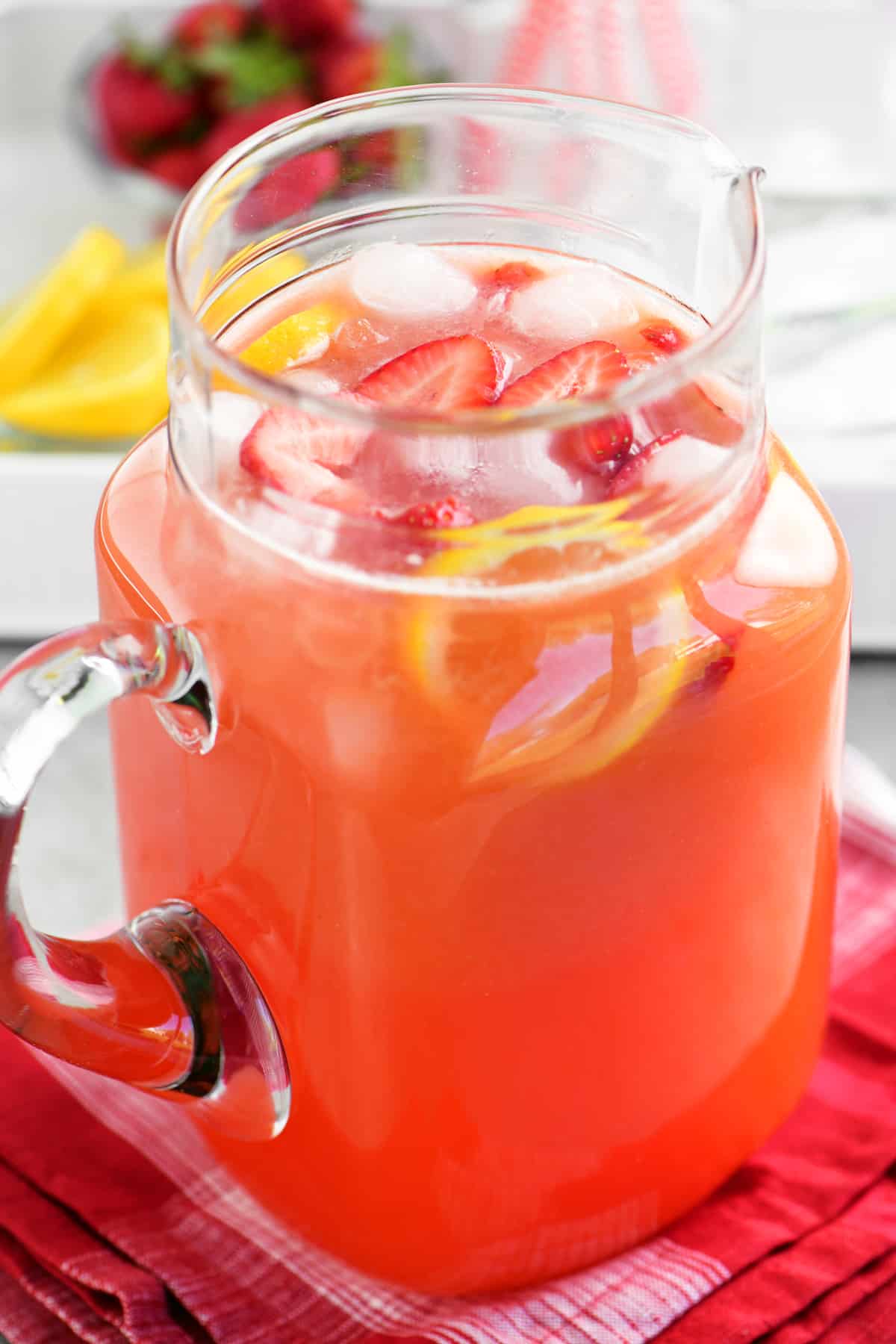 a glass pitcher with lemonade, strawberries and lemons inside