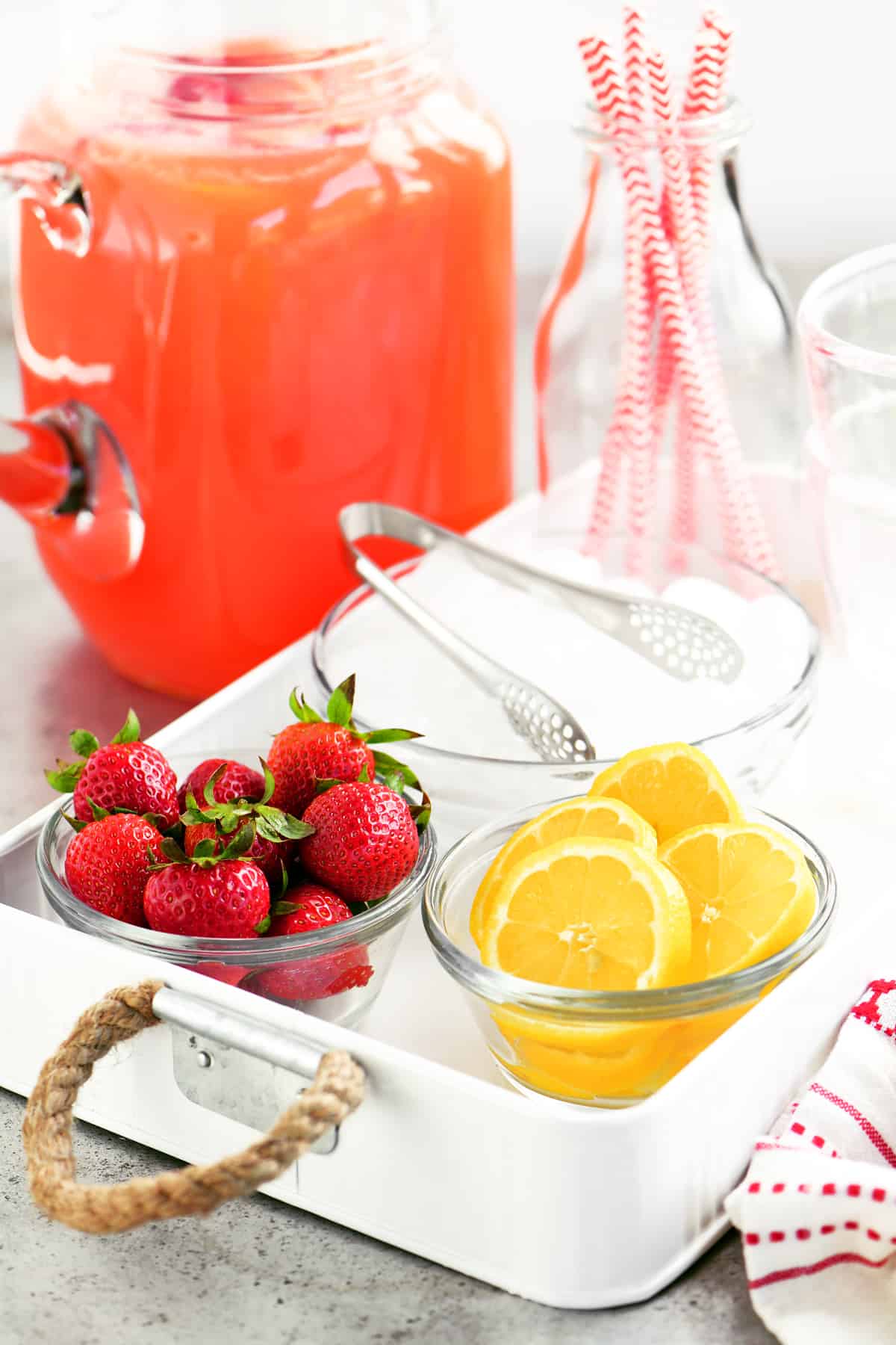 strawberry lemonade in a pitcher next to a tray with strawberries and lemons and ice