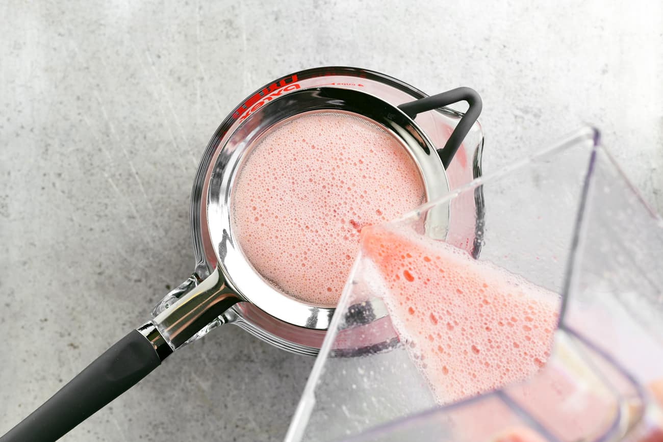 pouring blended strawberries through a strainer