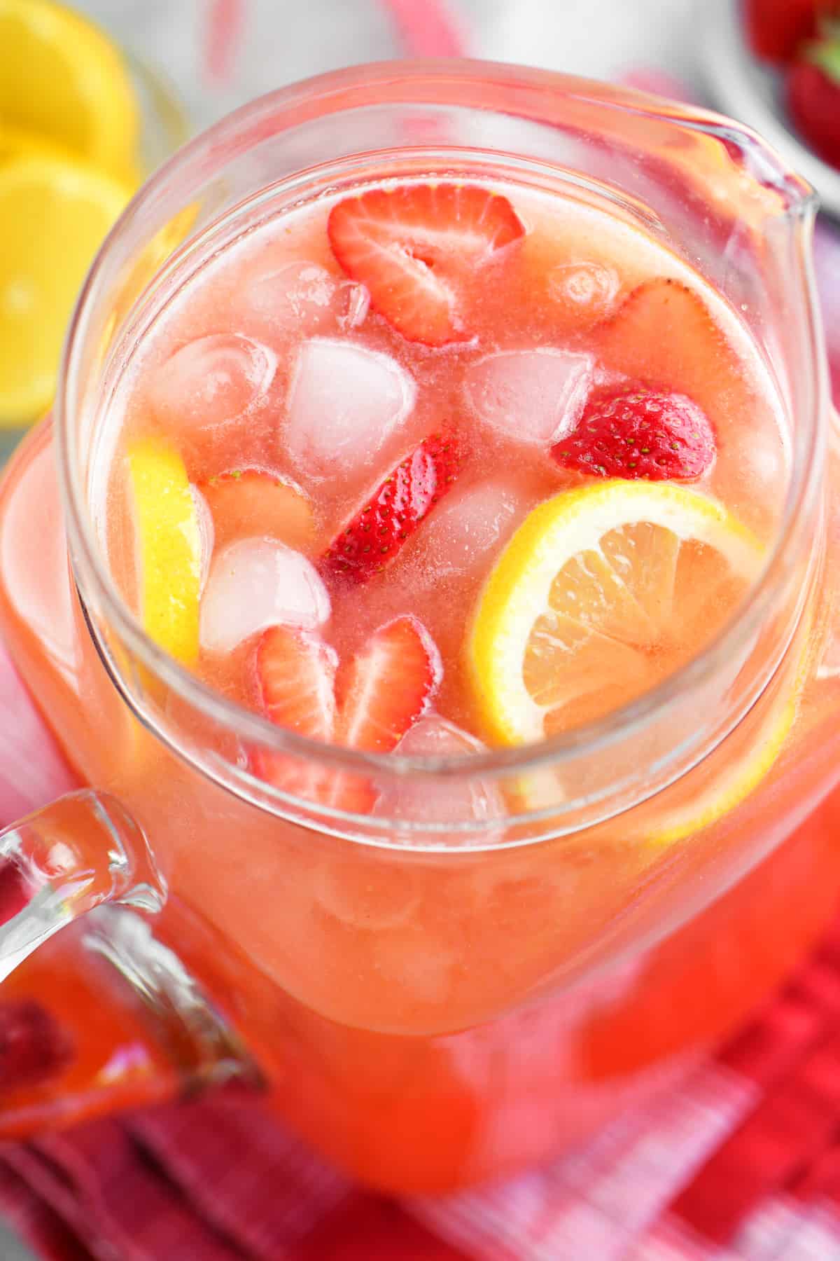 a pitcher of lemonade with lemons and strawberries and ice inside