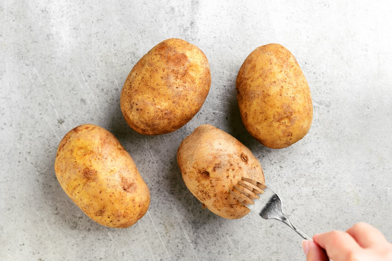 a hand poking holes into a potato with a fork