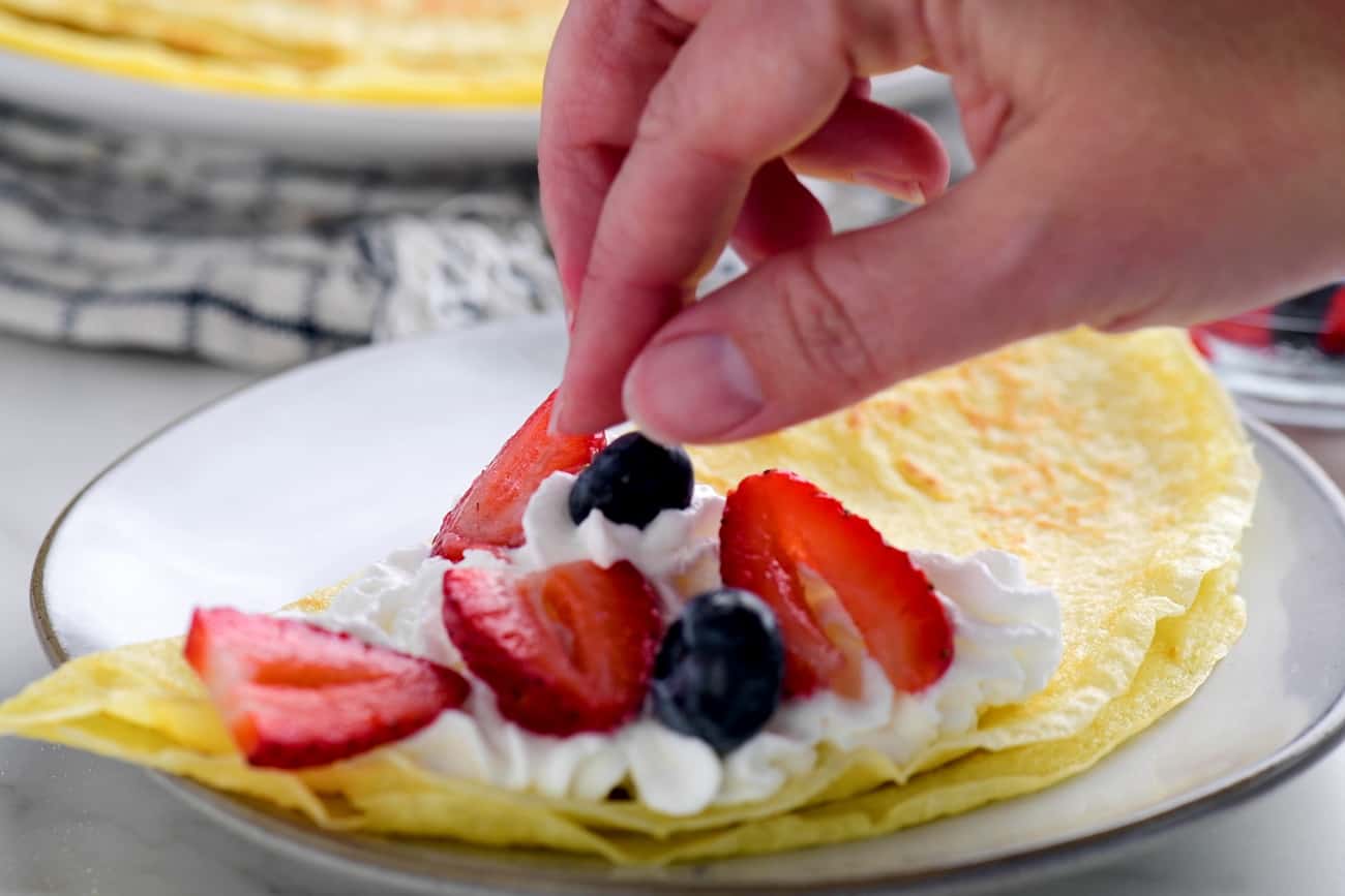 a hand adding berries to the top of the whipped cream