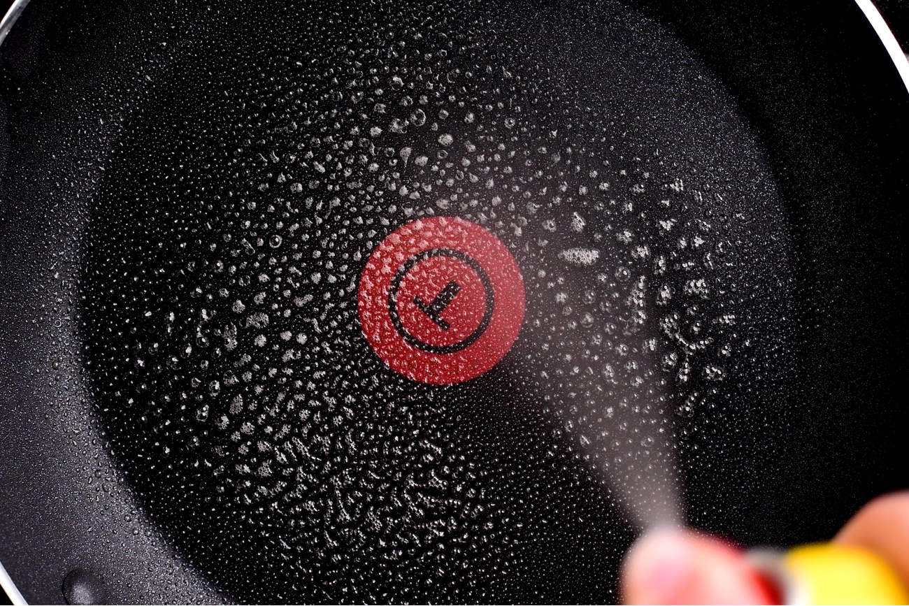a hand spraying cooking spray on a frying pan
