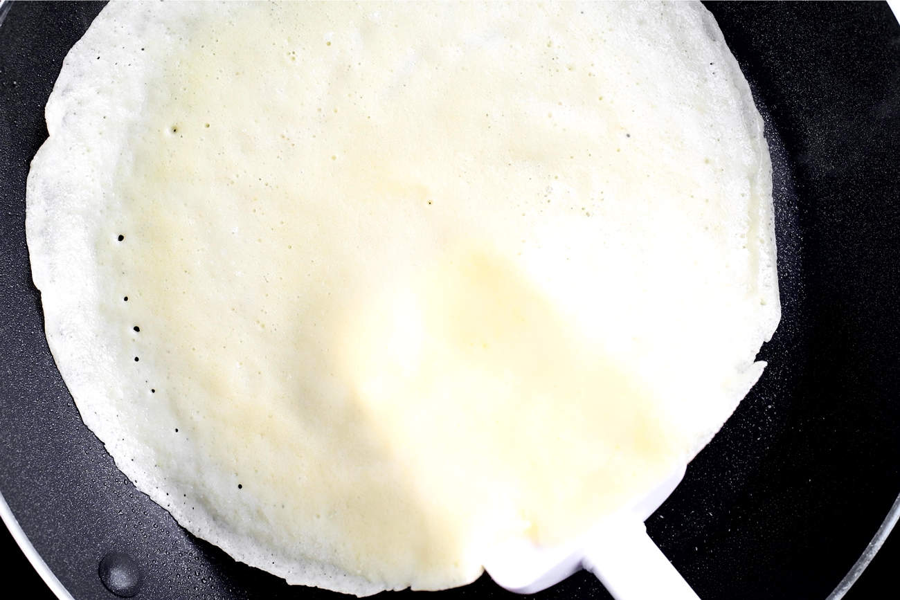 a white spatula lifting a crepe in a frying pan