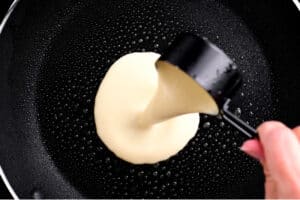 a hand pouring batter into a frying pan
