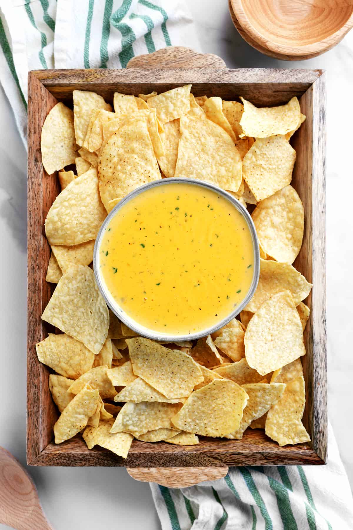 wooden tray with queso in a bowl surrounded by tortilla chips