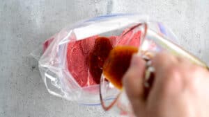 pouring marinade on a steak in a gallon sized ziptop bag