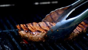 placing a steak on the grill with tongs