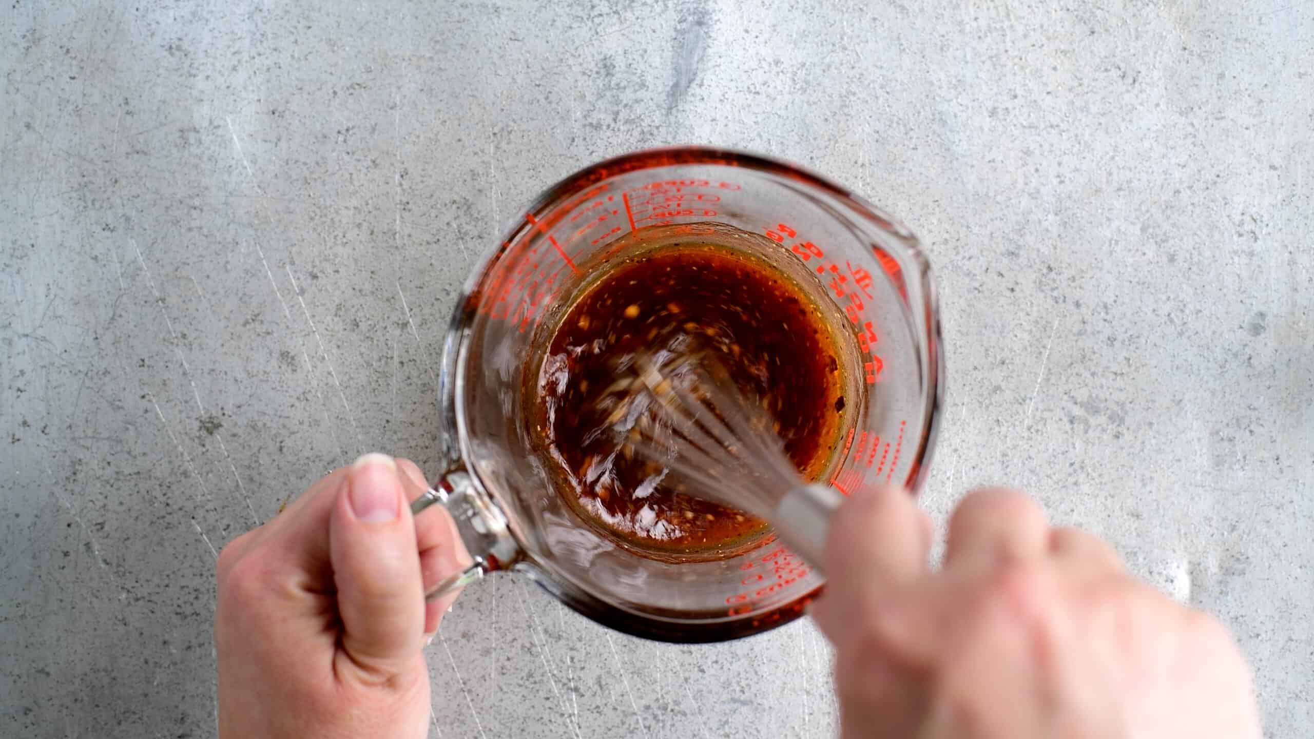 whisking steak marinade in a glass measuring cup