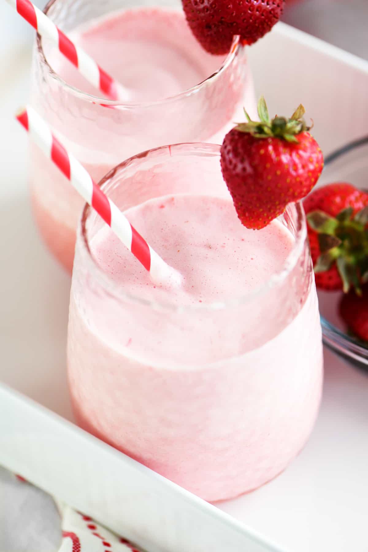 two glasses of strawberry whip with a strawberry garnish and striped straw
