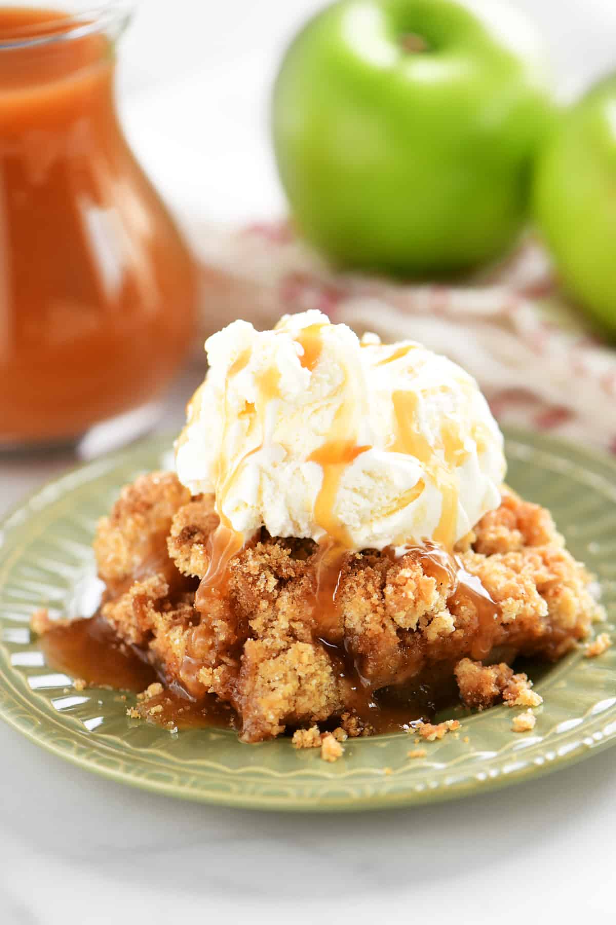 slice of apple crumble on a green plate with vanilla ice cream and caramel on top