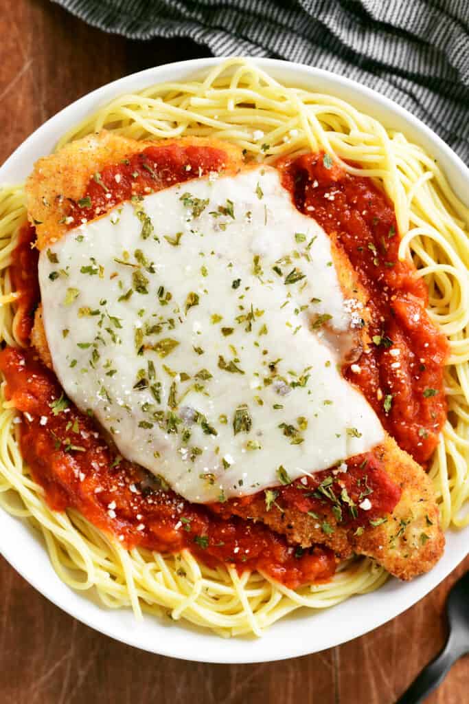 chicken parmesan on spaghetti noodles in a white bowl