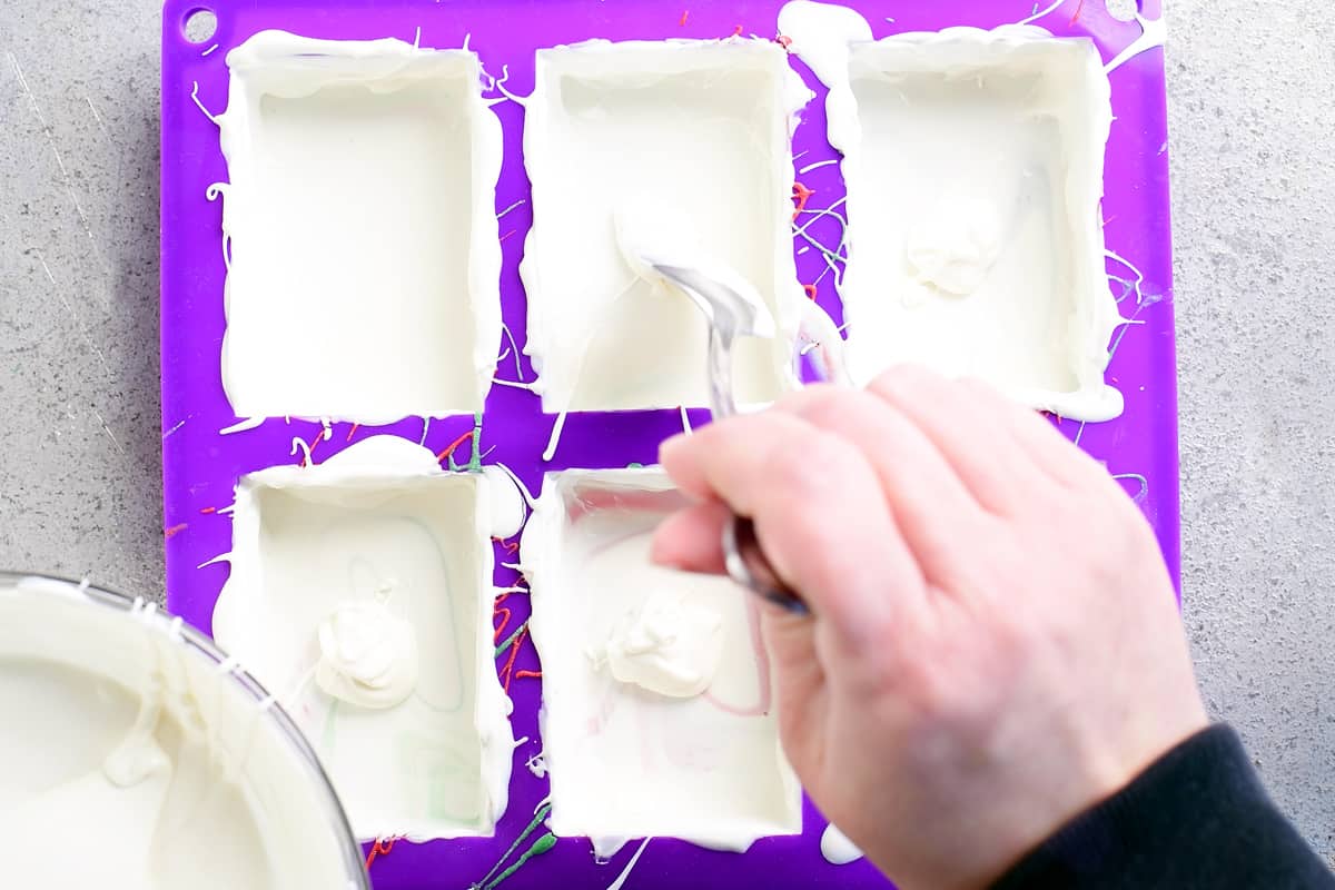 adding melted white chocolate to a purple silicone mold