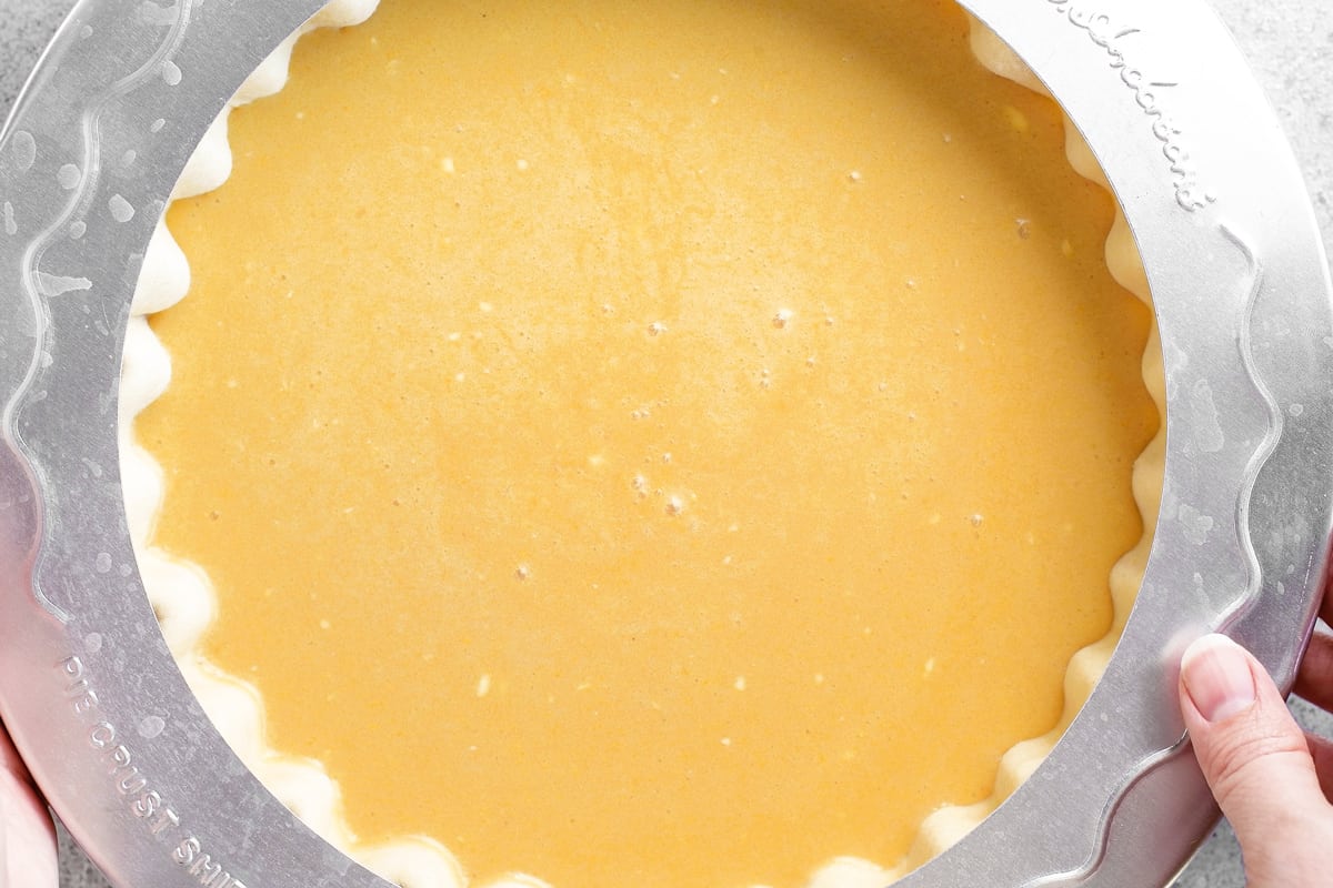 hands placing a pie ring onto the chess pie prior to baking