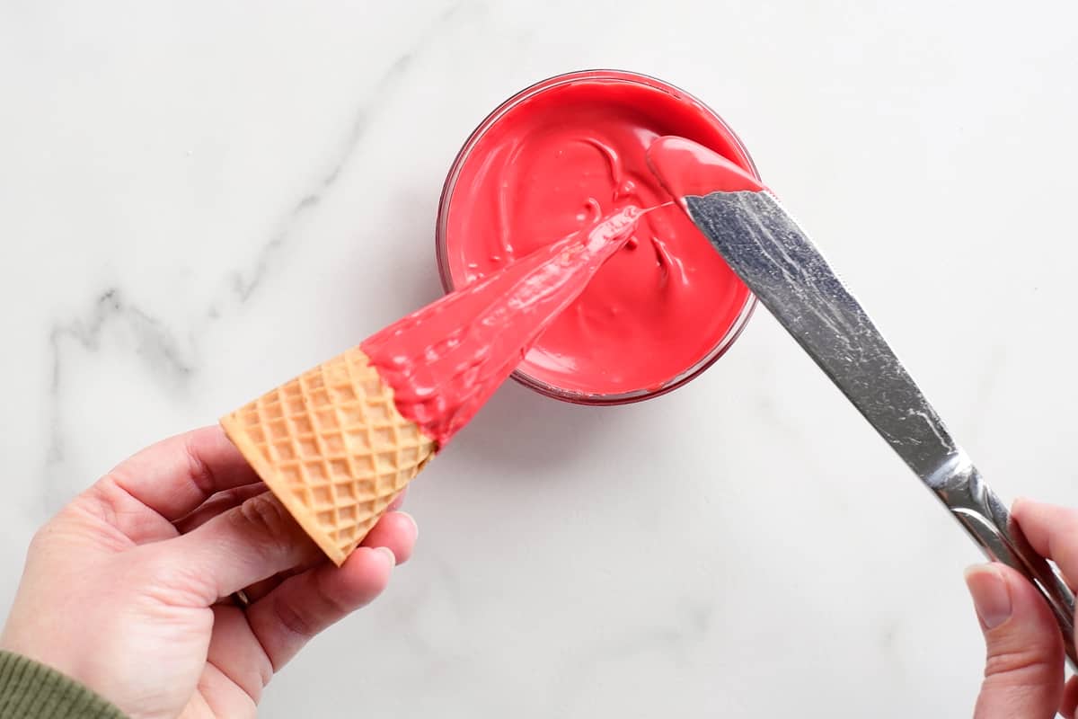 applying red icing to an ice cream cone with a knife